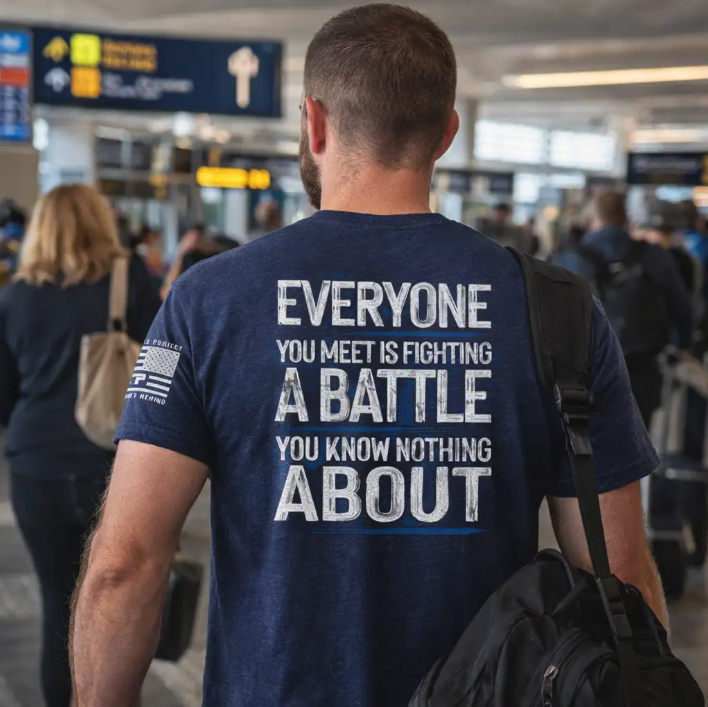 Traveler walking through an airport wearing a shirt that reads “Everyone you meet is fighting a battle you know nothing about.”